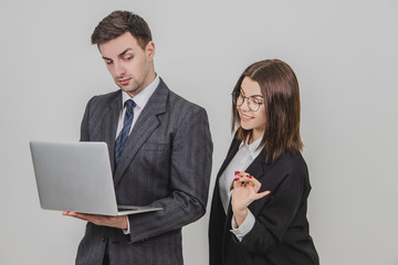 Handsome man standing, working with laptop. Woman is pointing from man's behind at something in the...