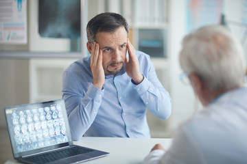 Mature man complaining o headache to the doctor while sitting at the table at doctor's office