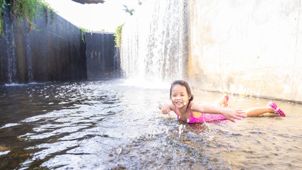 happy little asian girl playing water in spillway of weir