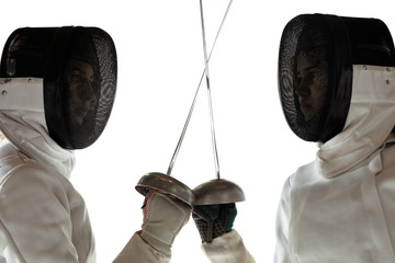 Standoff. Close up of teen girls in fencing costumes with swords in hands on white background....