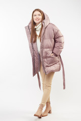 Beautiful sexy pretty girl with long brown hair and perfect body weared in beige leather pants and white sweater, jasmine down jacket, boots. Isolated on white background.