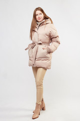 Beautiful sexy pretty girl with long brown hair and perfect body weared in beige leather pants and white sweater, beige down jacket, boots. Isolated on white background.