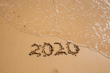 Summer beach holiday 2020 season golden sand - year - decade - new season lettering on the beach with wave and clear blue sea. Numbers 2020 year on the sea shore, message handwritten New Years concept