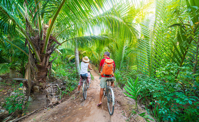 Tourist couple riding bicycle in the Mekong Delta region, Ben Tre, South Vietnam. Woman and man...