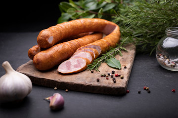 Rings of traditional, country, homemade, pork smoked sausage on a wooden cutting board on a stony countertop.