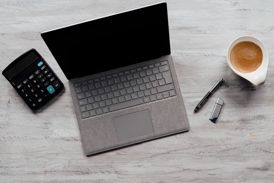 Geöffneter Laptop auf einem Schreibtisch mit einem Taschenrechner, Kugelschreiber und einer Kaffeetasse 
