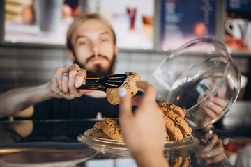 close up photo of a bakery worker who helps with the choice of ordering a buyer, takes oatmeal cookies out of a plate, demonstrating quality service, selective focus