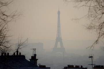 View of the Eiffel Tower and Parisian rooftops. Fog in the air caused by pollution. 