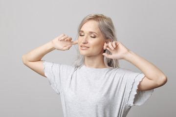Blond woman closed her ears by hands in the white studio