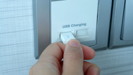 Hand plugging in a USB cable into a wall mounted USB charging port.