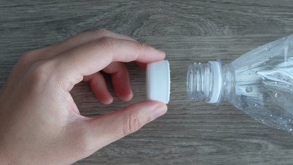 Closeup of the mouth of a clear plastic bottle, with a hand holding the white cap.