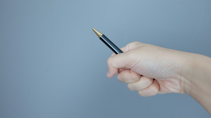 Hand gripping on a ball pen and pointing it at an angle, with copy space on the left.