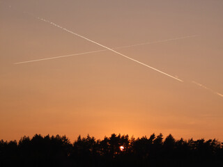 Two jet trails painting a beautiful abstract painting into the orange sunset sky above a forest in Franconia / Bavaria, Germany