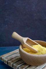 Dry uncooked corn polenta in a wooden bowl with spoon on dark background. Copy space, close up image. Traditional Italian food, vegan and healthy food concept. Natural light.
