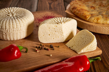 Sliced round white homemade cheese - traditional milk creamy dairy product on vintage wooden board. Rustic style. Feta cheese served with red peppers on vintage wooden board National Georgian cuisine
