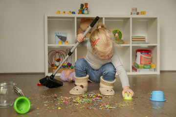 Adorable blonde toddler girl playing with broom, cleaning colorful confetti from the floor - obrazy, fototapety, plakaty