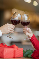 A couple sitting in a restaurant and crossed their wineglasses. A giftbox and a beautiful rose on the table. A man and a woman having drinking wine at a cafe. Valentine's day concept.
