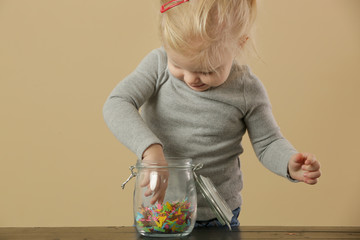 Adorable toddler girl playing with a jar full of confetti