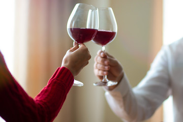 A cheerful young couple crossing their wineglasses at a restaurant. A man and his girlfriend drinking wine at a cafe. Red rose on a table. Valentine's day concept.