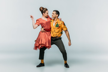 young dancer holding partner while dancing boogie-woogie on grey background
