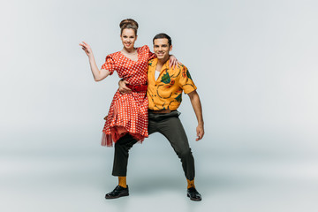 handsome dancer holding partner while dancing boogie-woogie on grey background