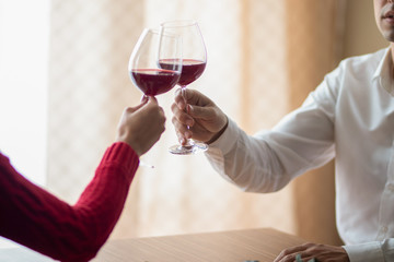 A cheerful young couple crossing their wineglasses at a restaurant. A man and his girlfriend drinking wine at a cafe. Red rose on a table. Valentine's day concept.