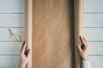 Female hands unfolding a roll of wrapping brown craft paper for packing gifts and flowers on the...