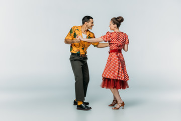 smiling dancers looking at each other while dancing boogie-woogie on grey background