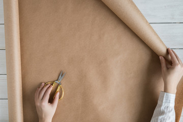 Female hands unfolding a roll of wrapping brown craft paper for packing gifts and flowers on the...