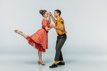 cheerful dancers holding hands while dancing boogie-woogie on grey background