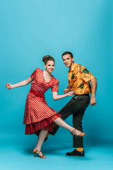 cheerful dancers looking at camera while dancing boogie-woogie on blue background