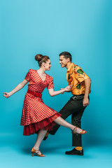 smiling dancers looking at each other while dancing boogie-woogie on blue background