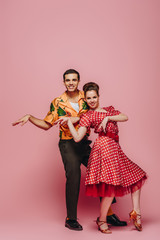 stylish dancers looking at camera while dancing boogie-woogie on pink background