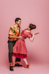 stylish dancers looking at each other while dancing boogie-woogie on pink background