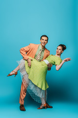handsome dancer supporting girl while dancing boogie-woogie on blue background