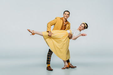 handsome dancer supporting partner while dancing boogie-woogie on grey background