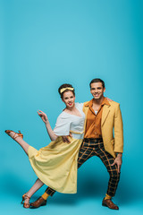 stylish dancers looking at camera while dancing boogie-woogie on blue background