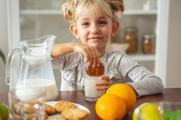 Cute little girl dipping cookie in milk - Powered by Adobe