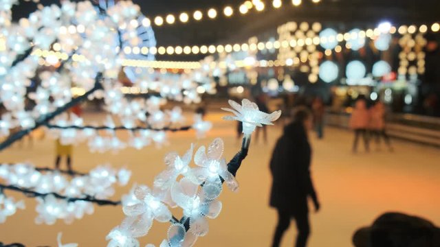 Ice skating during Christmas holidays blurred. People skating on an outdoor skating rink in winter at night. Garlands on the foreground 4k