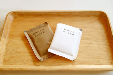 Bags of brown sugar and white sugar isolated on wooden tray