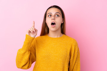 Teenager girl with yellow sweater over isolated pink background thinking an idea pointing the finger up