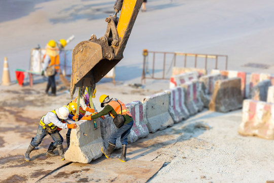 Many workers wear safety suits helped to lift and arrange the cement concrete barriers by excavator In harmony and actively on the road