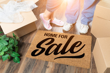 Man and Woman Standing Near Home For Sale Welcome Mat, Moving Boxes and Plant
