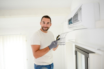 handsome young man electrician cleaning air filter on an indoor unit of air conditioning in a client house