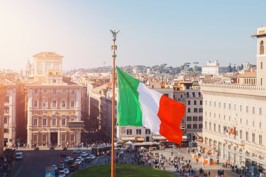National flag of Italy is developing in wind, background cityscape of Rome summer