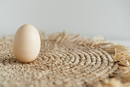 minimalism, one chicken egg on a light background and a straw napkin
