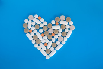 Symbol heart from pills and capsules on medicine blue background
