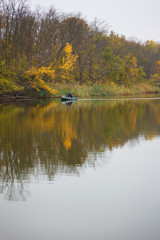 The boat floats by the river through the autumn forest.