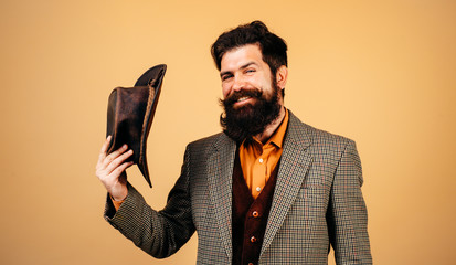 Cheerful smiling gentleman takes off hat in salutation isolated at orange background. Handsome...