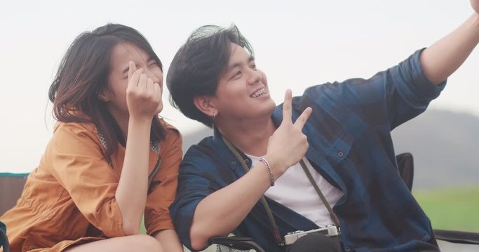 Young asia campers couple camping near relax enjoy love moment seaside. Male and female traveler using smartphone taking selfie at campsite. Outdoor activity, adventure travel, or holiday vacation.